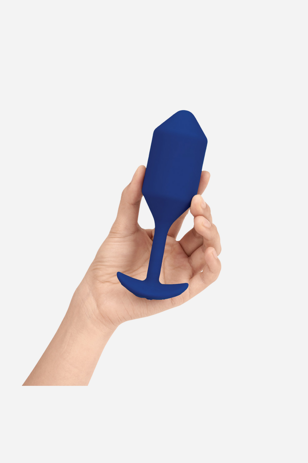 Hand holding the B-Vibe Vibrating Snug Plug 4 in Navy, showing its weighted bulb, slim neck and flared base on light grey