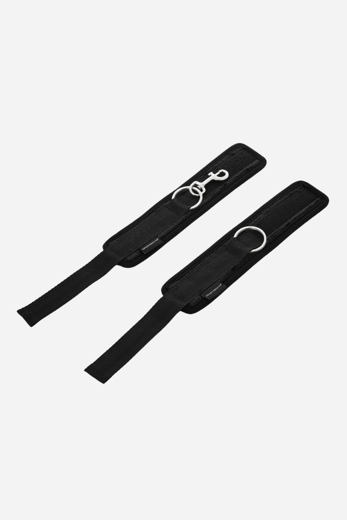 The two black cuffs laid open and flat on grey, showing the full length of each strap and the loop backing that fastens them.