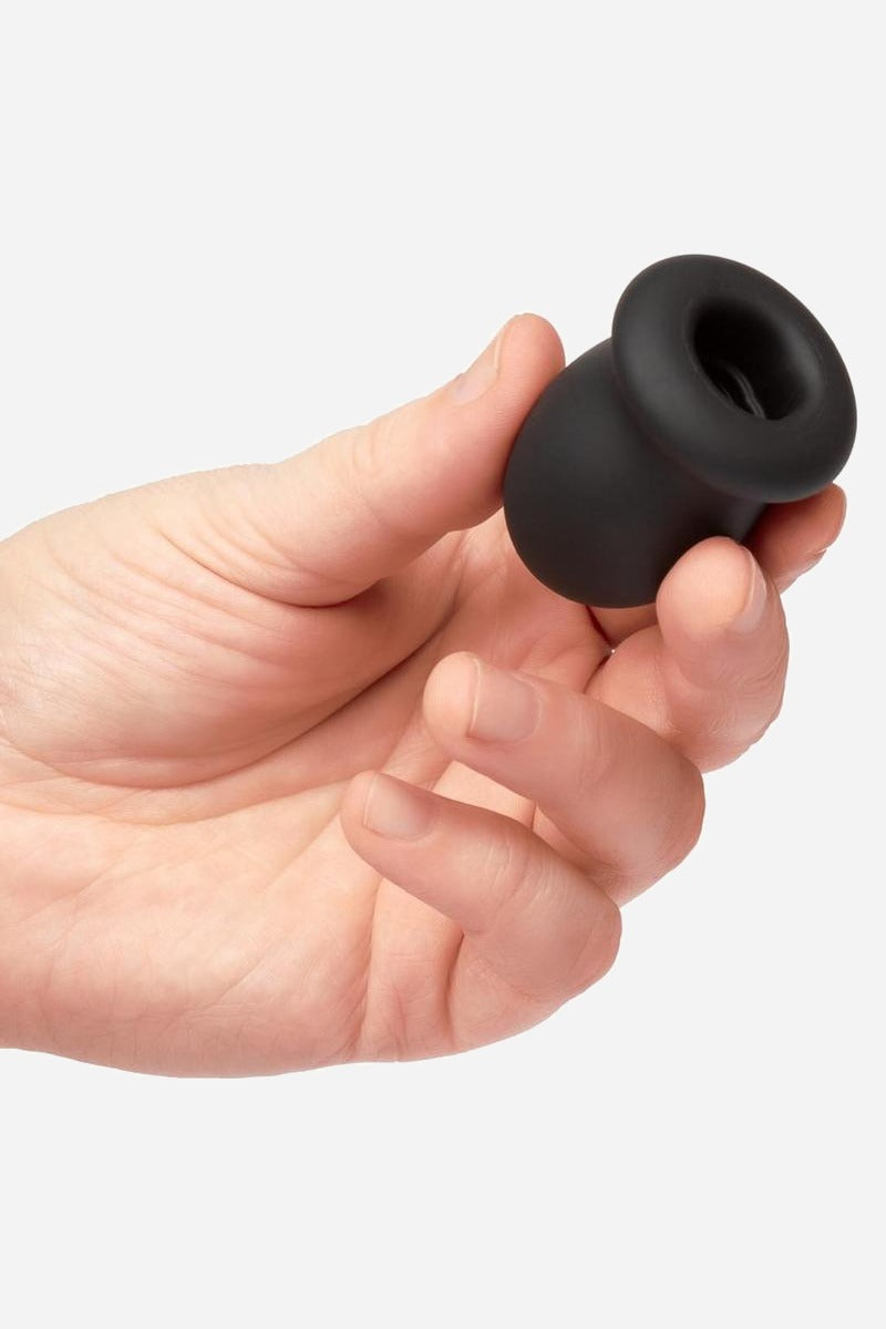 Hand holding the small black Boundless FTM silicone stroker between thumb and fingers, showing its open ribbed end and flared base