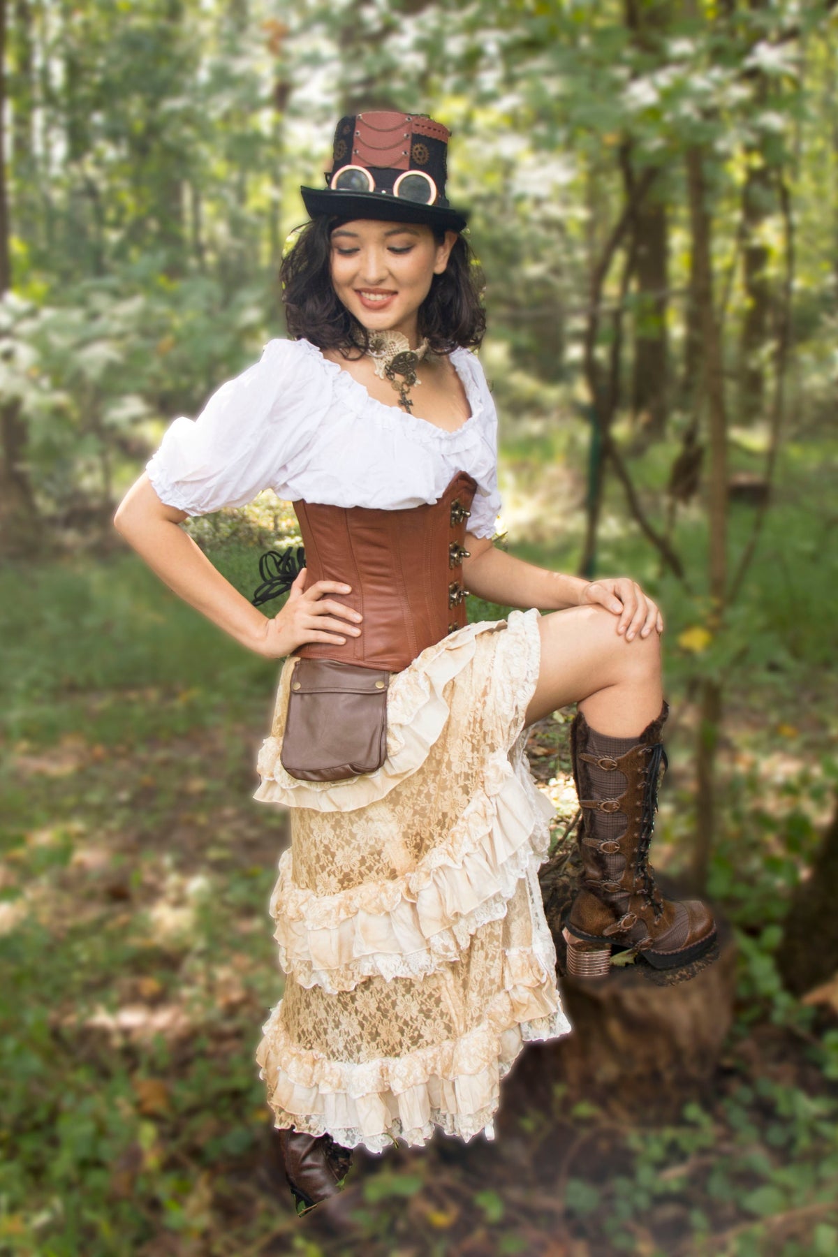 Model in a steampunk outfit with top hat, white blouse and ruffled skirt wearing the natural leather Cersei corset in a forest