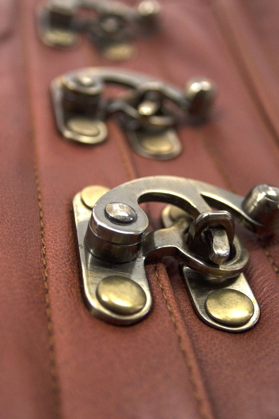 Close-up of the antique brass hook clasps on the front busk of the Cersei corset against smooth natural tan leather