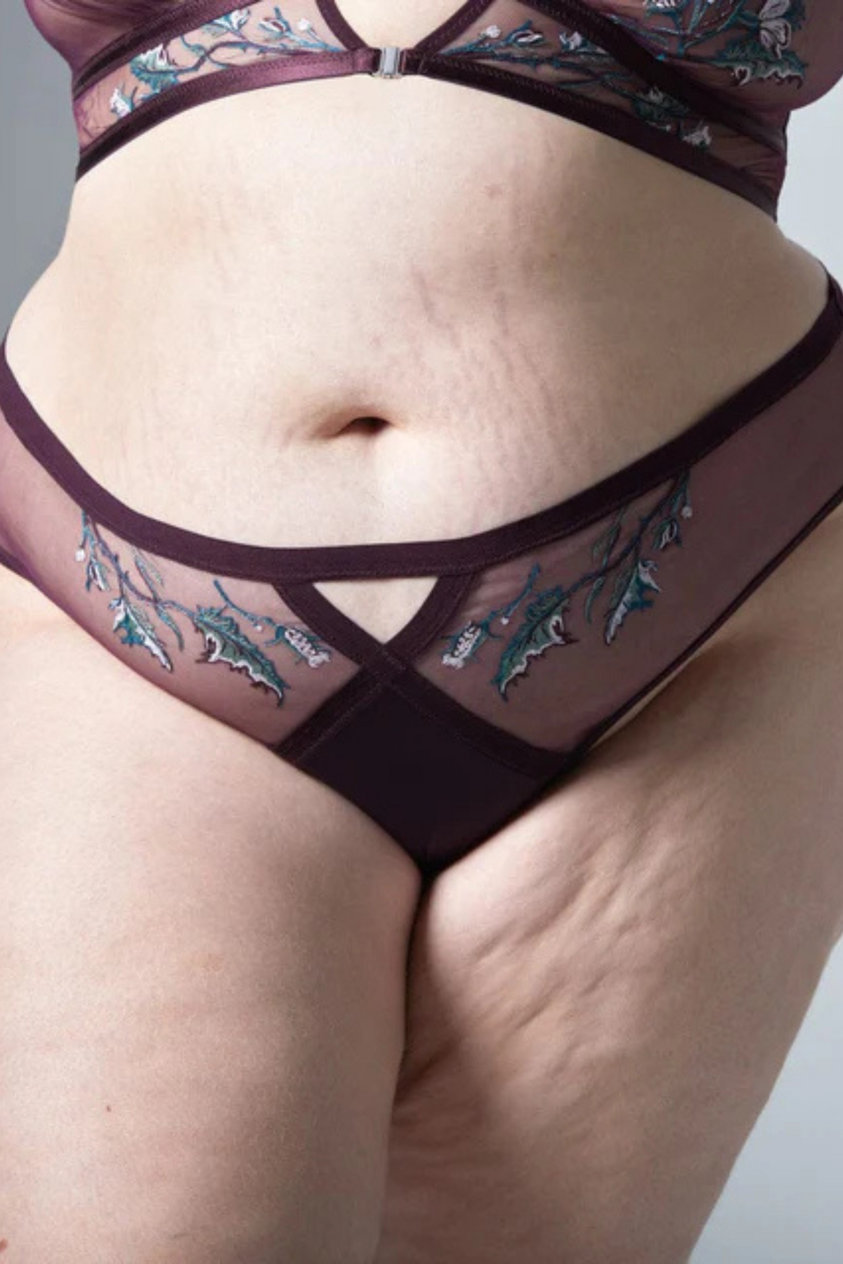 Plus-size model in the Cirsi the Sorceress bikini in cordial plum with sheer mesh, a center keyhole cut-out and witchy embroidery