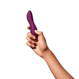 view of a brown hand holding the dame dip sex toy upwards. toy is slightly longer than a palm of a hand