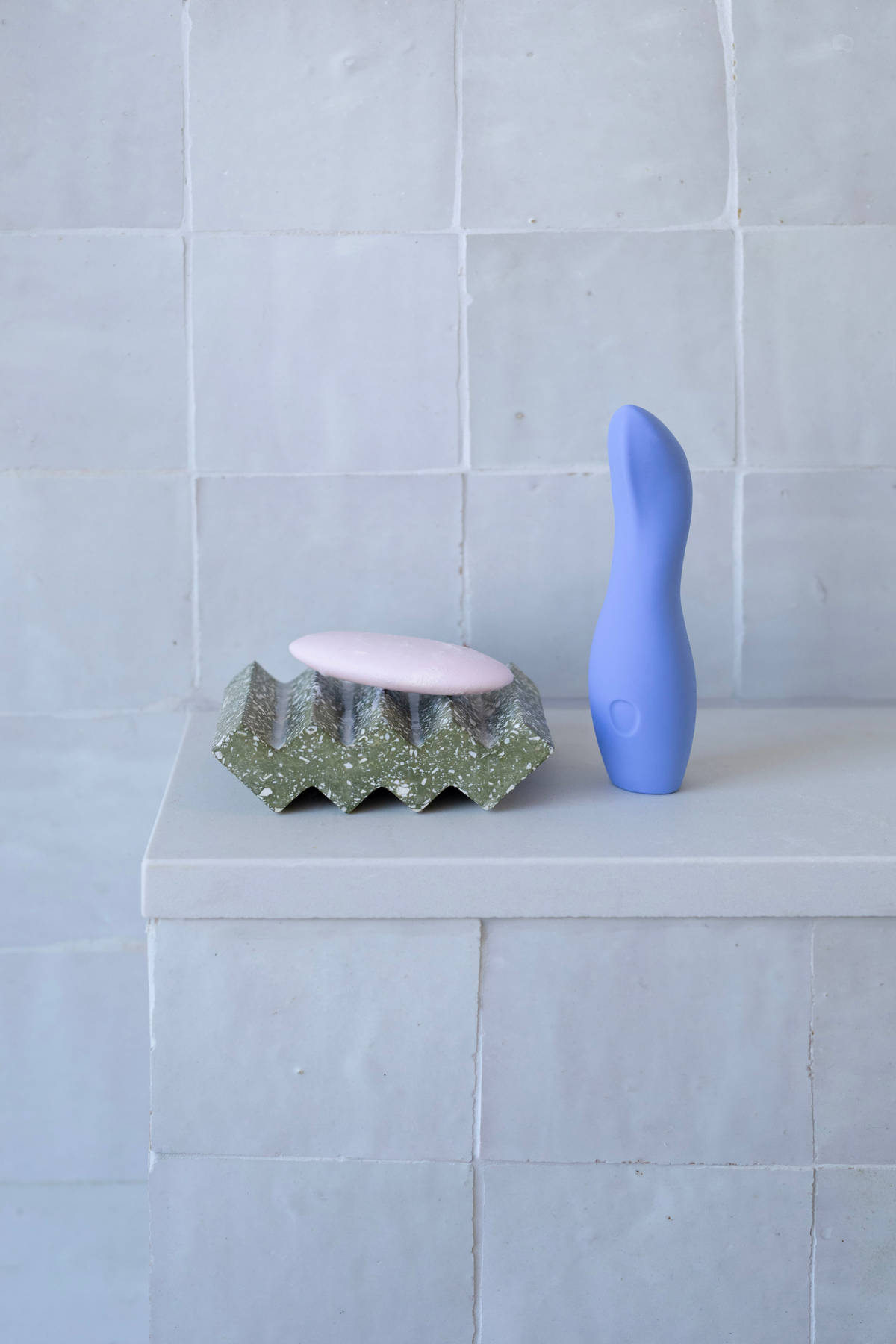 Periwinkle Dame Dip 2.0 palm vibe standing on a tiled bathroom shelf beside a sculpted soap dish, a lifestyle shot of its discreet design