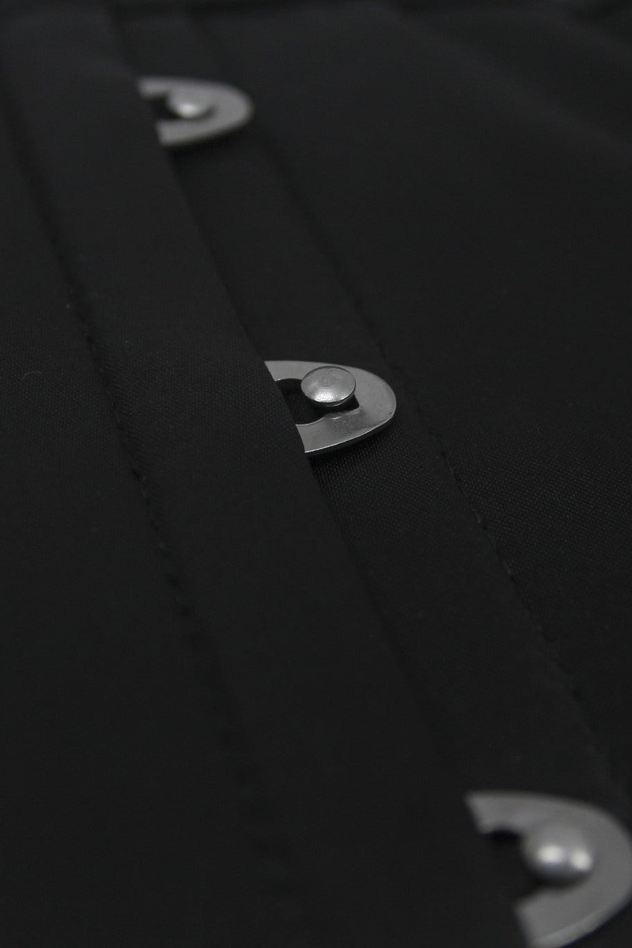Close-up of the silver busk clasps on the front of the black Discreet Rendezvous waist cincher, showing the stitched seams