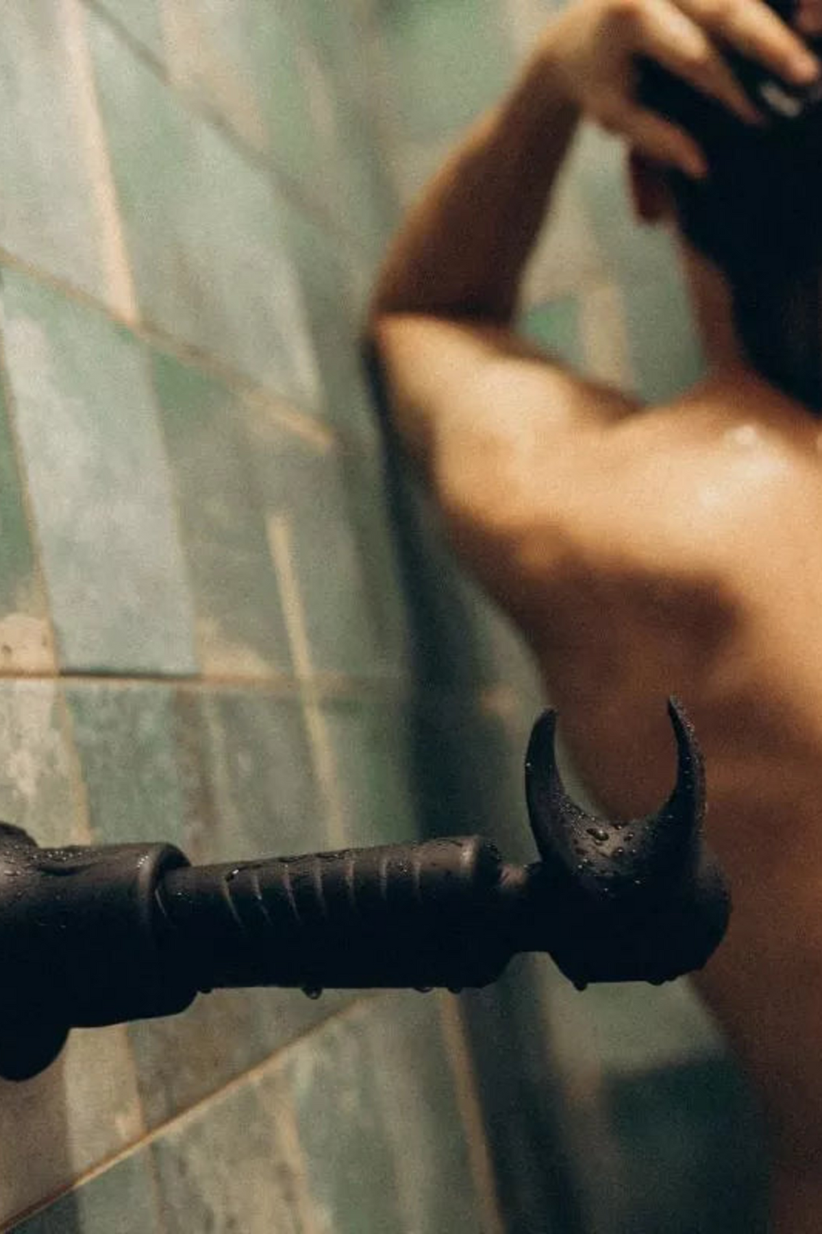 A person seen from behind in a green tiled shower, with the black Evo stroking wand shown large in the foreground of the frame.