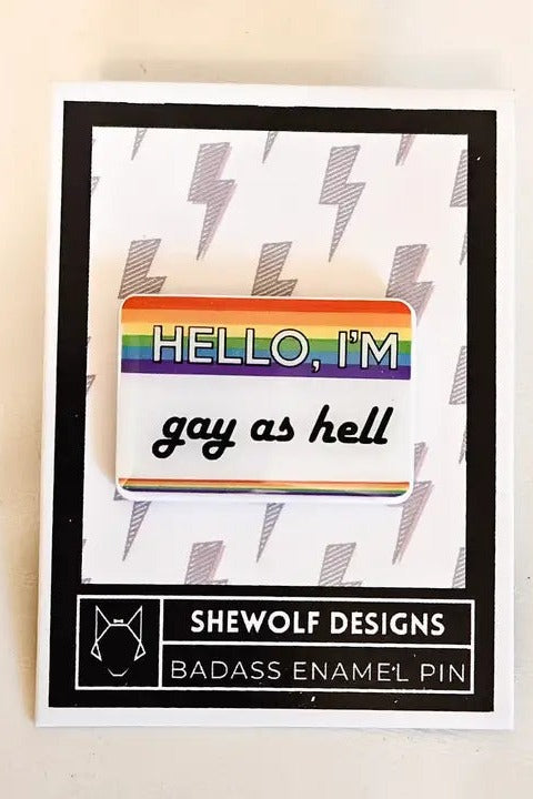 Hello I'm gay as hell rainbow name tag enamel pin mounted on a white SheWolf Designs backing card with grey lightning bolts and a black border