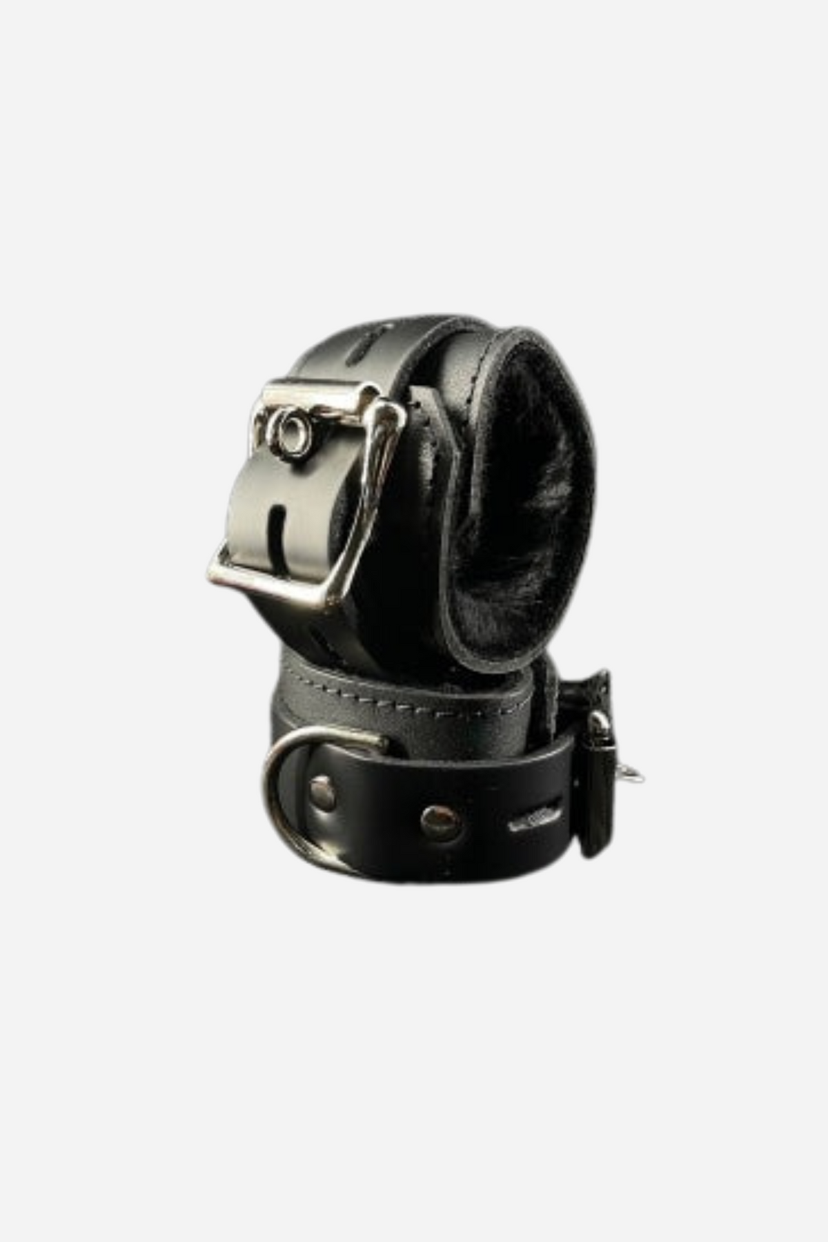 Two black leather wrist cuffs lined with soft black fleece, one resting behind the other, with silver buckles and D-rings, on a grey backdrop.