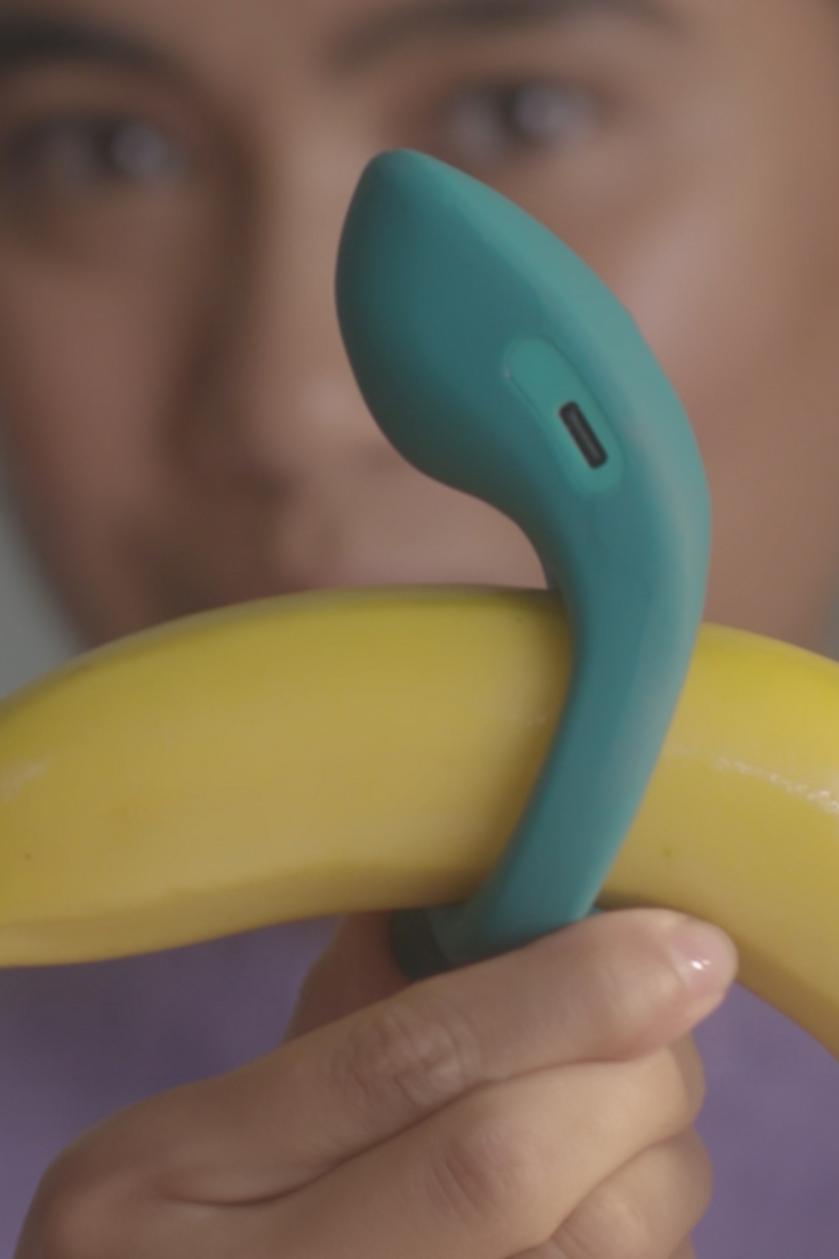 Person holding the Dame Hug vibrating cock ring around a banana to show how the ring fits snugly and where the vibrating arm sits