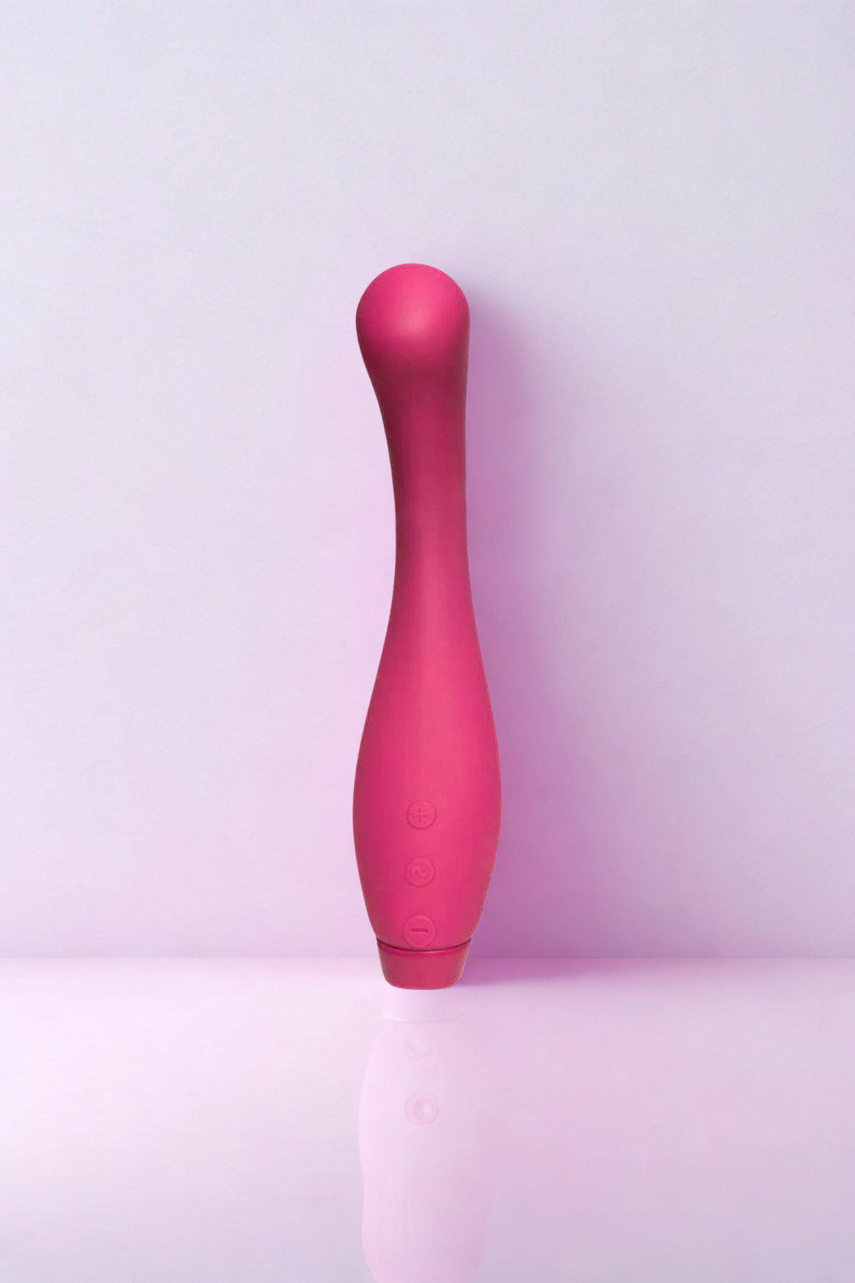 Je Joue Juno G-spot vibrator in Fuchsia standing on a reflective surface against a soft pink and lilac backdrop, showing its shape