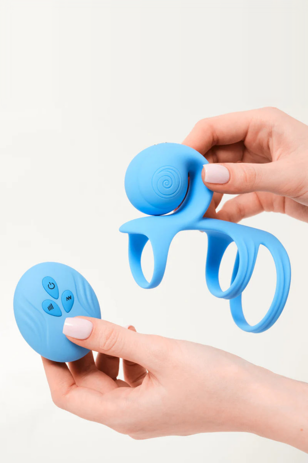 Hands holding the blue Jovi Tri Arc Cock Ring and its round remote control, showing the three-ring sheath and the remote's control buttons