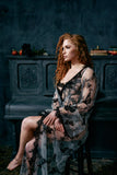 curly red haired model sits looking away in a regal mesh robe with black embroidery butterflies