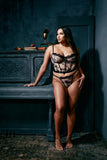 light skinned plus size black model with long straight hair stands next to piano wearing butterfly embroidered bustier and matching gstring