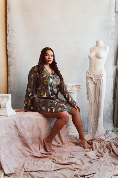 plus size light skinned model sits on a white painters cloth surrounded by italian-inspired roman statues, wearing Kilo Brava Satin Sleep Shirt in Iris & Swallows