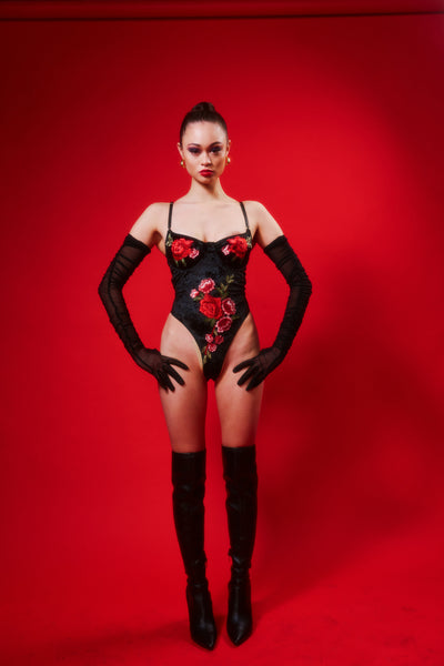 size small pacific islander model stands with hands on high thigh wearing the Kilo Brava Velvet Applique Underwire Teddy. Model is also wearing over the knee boots and long gloves. 
