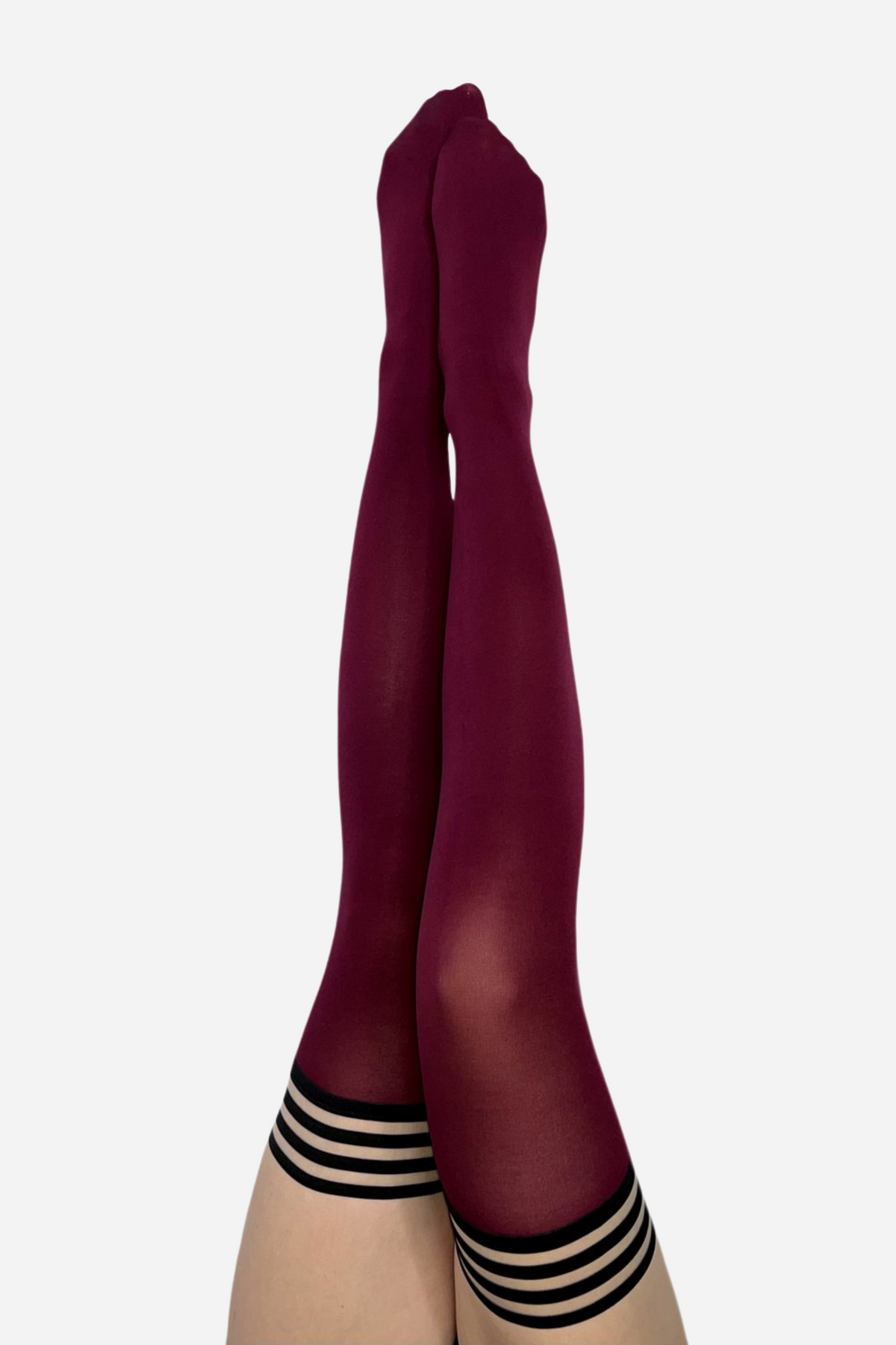 Legs raised together in deep cabernet opaque thigh highs, each stocking finished at the top with a band of narrow horizontal stripes.