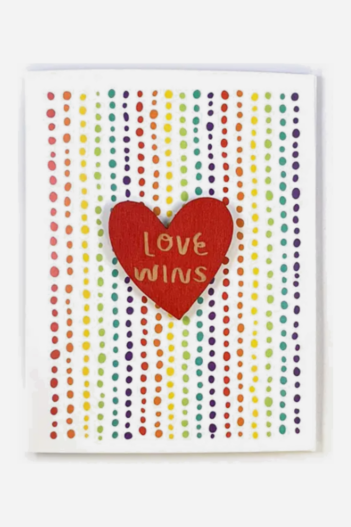 White greeting card covered in vertical rows of rainbow dots, with a red heart-shaped magnet reading Love Wins in gold lettering at the center