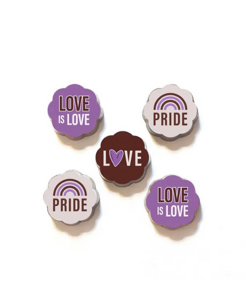 shows 5 flower shaped chocolates with pride themed designs in various shades of purple. two read "love is love" two have a purple rainbow with "pride" underneath, and one reads love with a heart for the "o"
