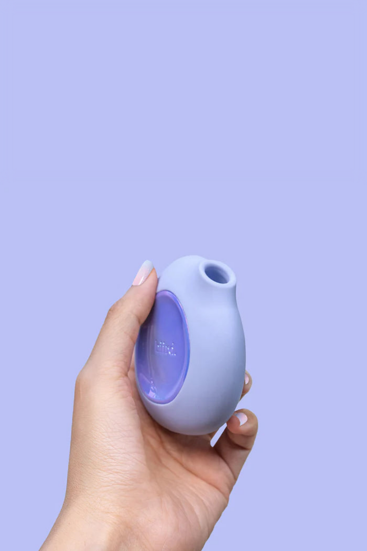 Hand holding the lilac Lumii air pulse toy against a lavender backdrop, showing how its rounded shape fits comfortably in the palm