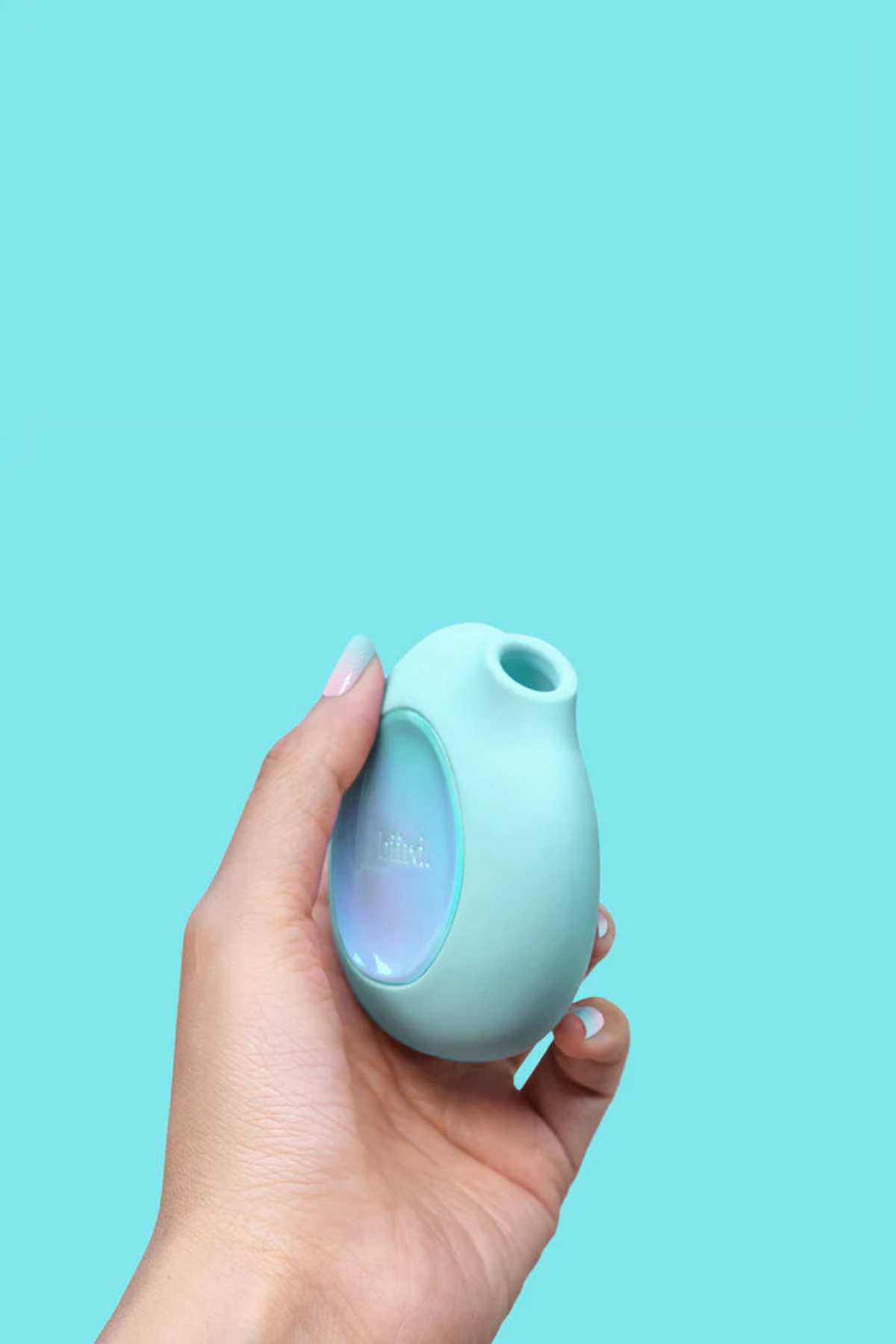 Hand holding the mint Lumii air pulse toy against an aqua backdrop, showing how its rounded shape fits comfortably in the palm