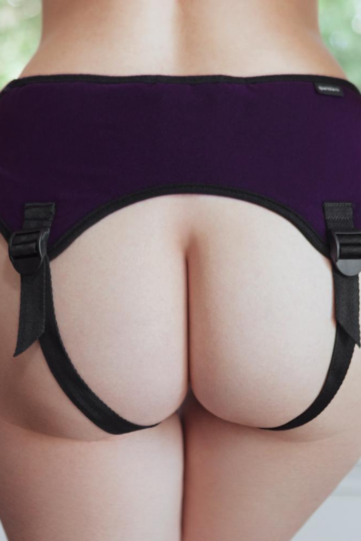 A model seen from behind wearing the purple Lush beginner harness, its black straps crossing each cheek and buckling at the sides.