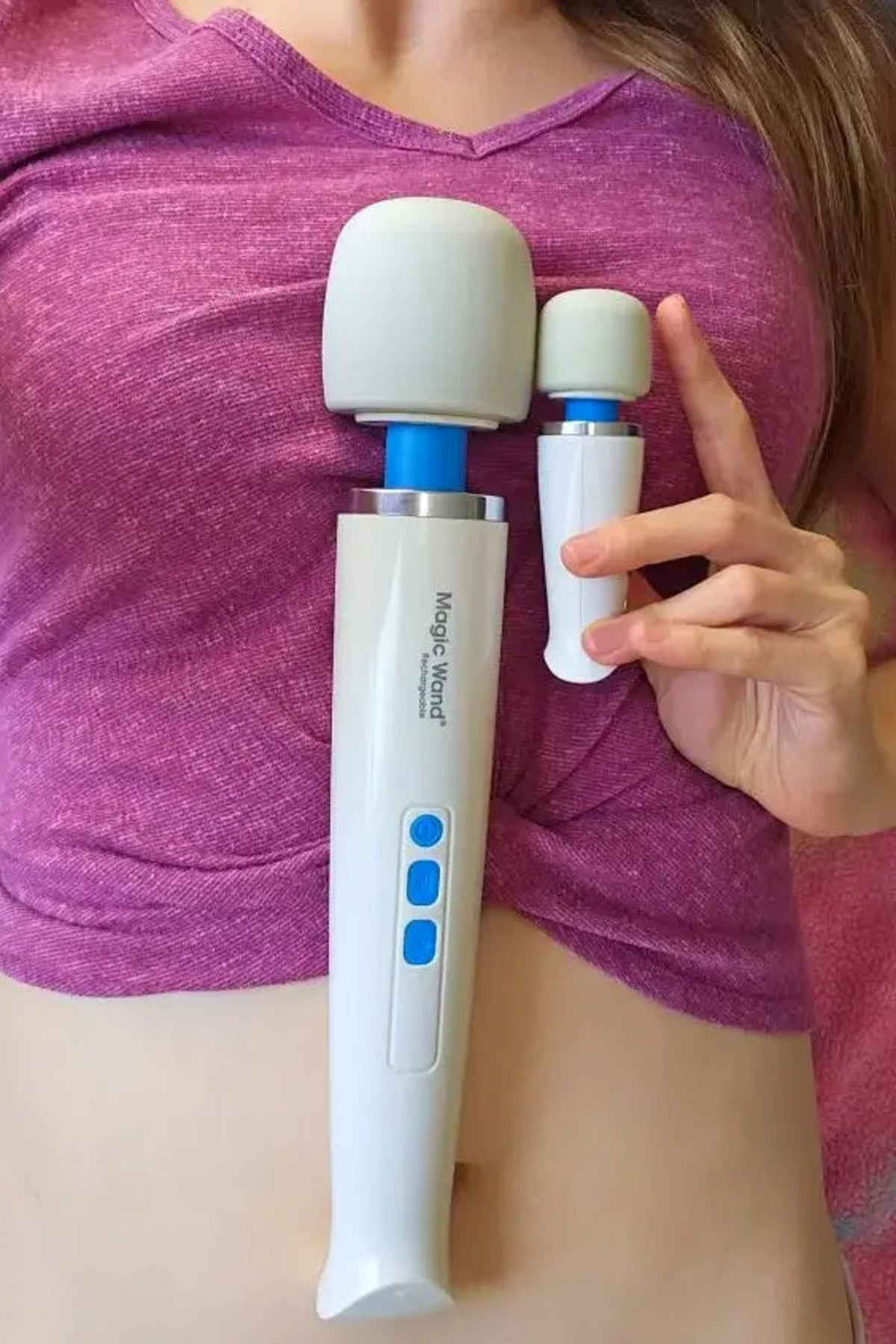 A model in a pink top holding the Magic Wand Micro against her hip beside a second larger wand, showing how small the Micro is.