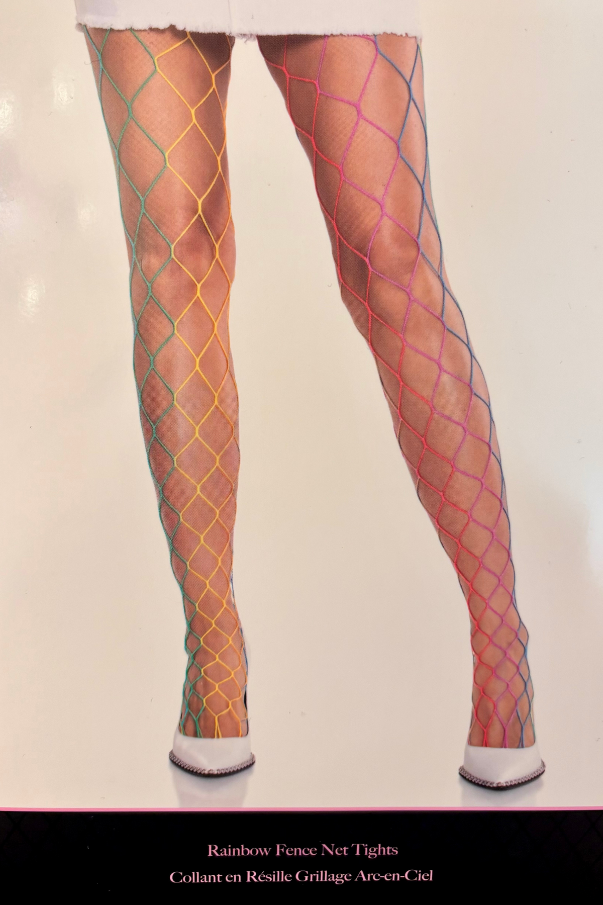 Legs in rainbow fence net tights worn with white shoes, the wide net striped through red, yellow, green and blue down the leg.
