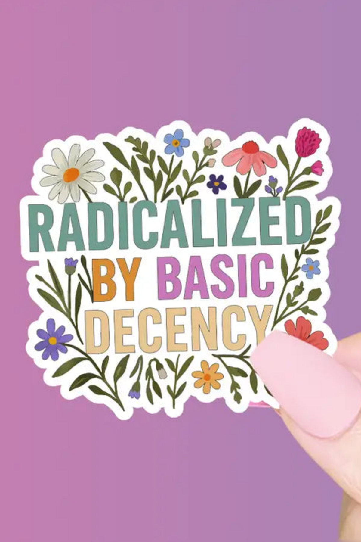 Hand holding a die-cut sticker reading Radicalized by Basic Decency in teal, pink and gold lettering wrapped in wildflowers, on a pink-purple backdrop