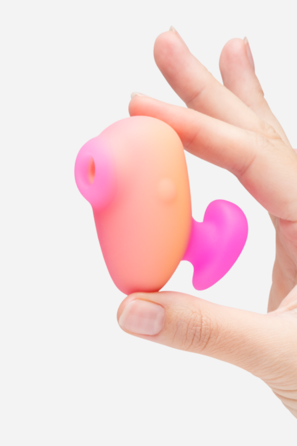 Hand holding the Romp Kiss clitoral suction toy in a peach to pink gradient, showing its compact travel-ready size and handle, on a grey background