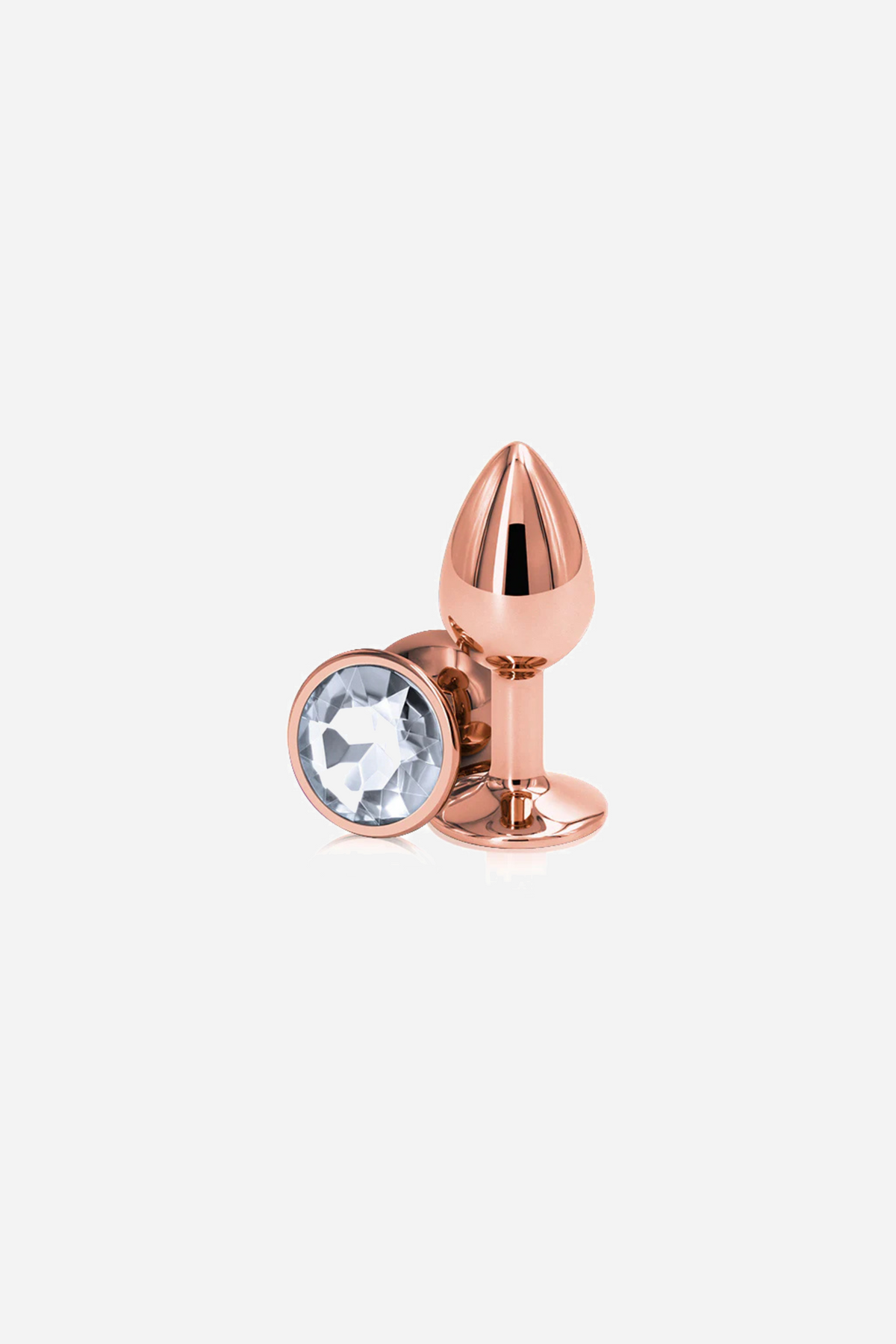 The small rose gold metal plug leaning against its round base, the base set with a clear faceted gem, shown on a plain backdrop