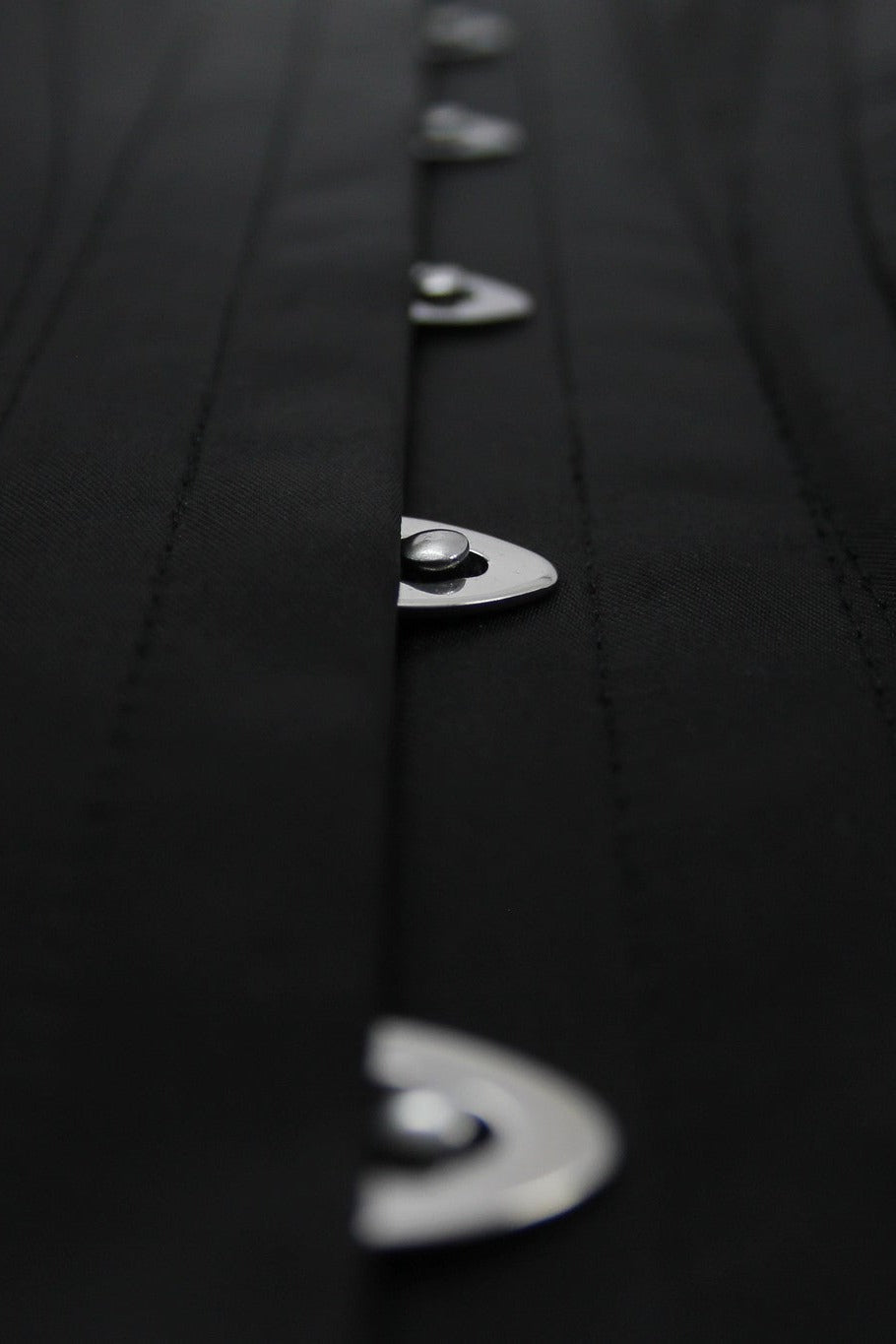 Close-up of the Seductress corset showing the black satin boning channels and silver busk clasps running down the centre front