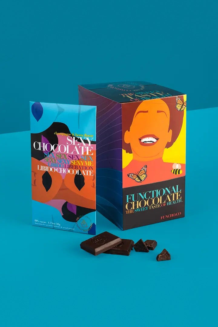 Sexy Chocolate bar in its illustrated wrapper beside the Functional Chocolate gift box and broken dark chocolate pieces on blue