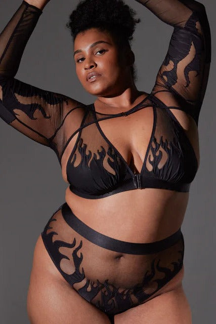 Plus-size model with arms raised in the black Smokin Mirrors sheer flame-print shrug worn over a matching bra and high-waist panty