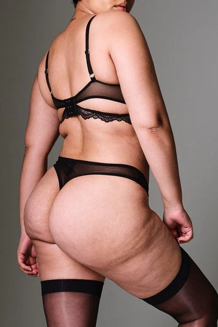 Back view of a curvy model in the black Sugar & Kane thong with strappy waistband, matching bra and black thigh-high stockings
