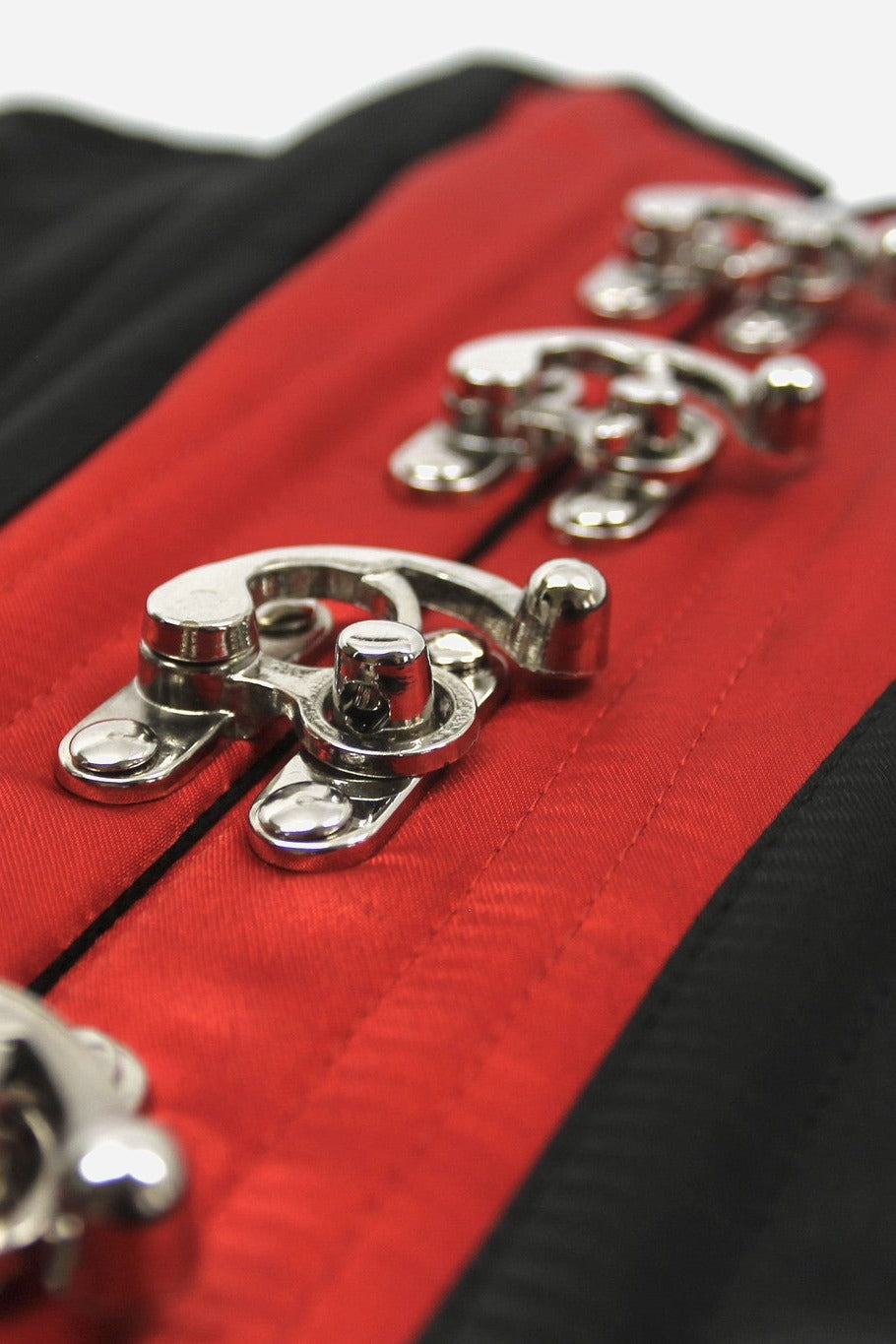 Close-up of the ornate silver hook clasps running down the red satin front panel of the black Tempest overbust corset