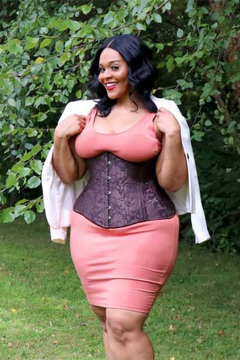 Model outdoors wearing the brown brocade Temptress underbust corset over a coral tank top and pencil skirt, with a white jacket on her shoulders