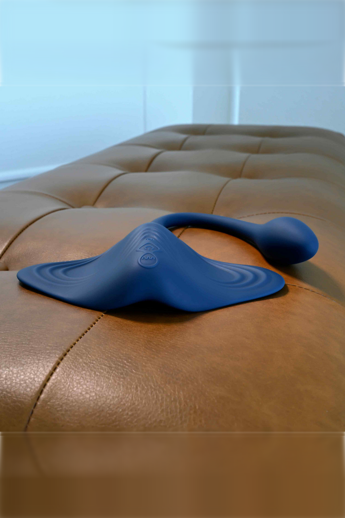 Navy Daily Grind Grinding & Stroking Pad resting on a tufted leather ottoman, showing its low profile for hands-free grinding play