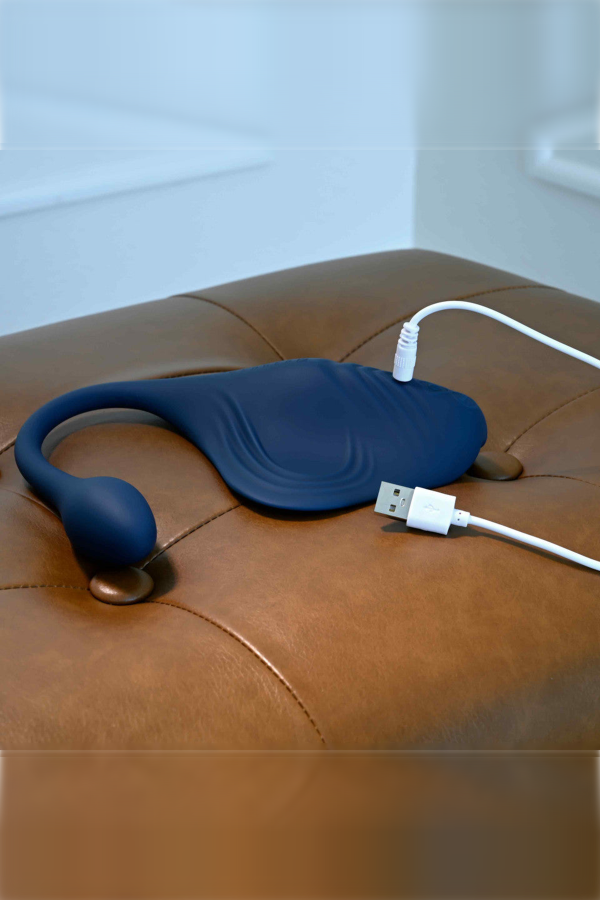 The Daily Grind pad on a leather ottoman with its USB charging cable alongside, showing the plug arm and the charging point on the pad