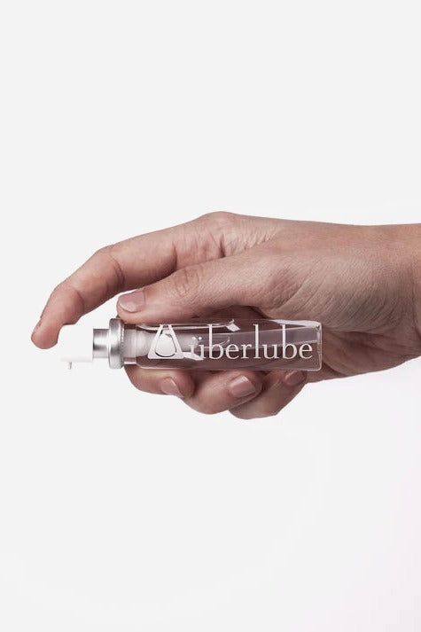 Hand holding the slim Überlube Good to Go 15ml travel spray bottle in clear glass with a silver pump top