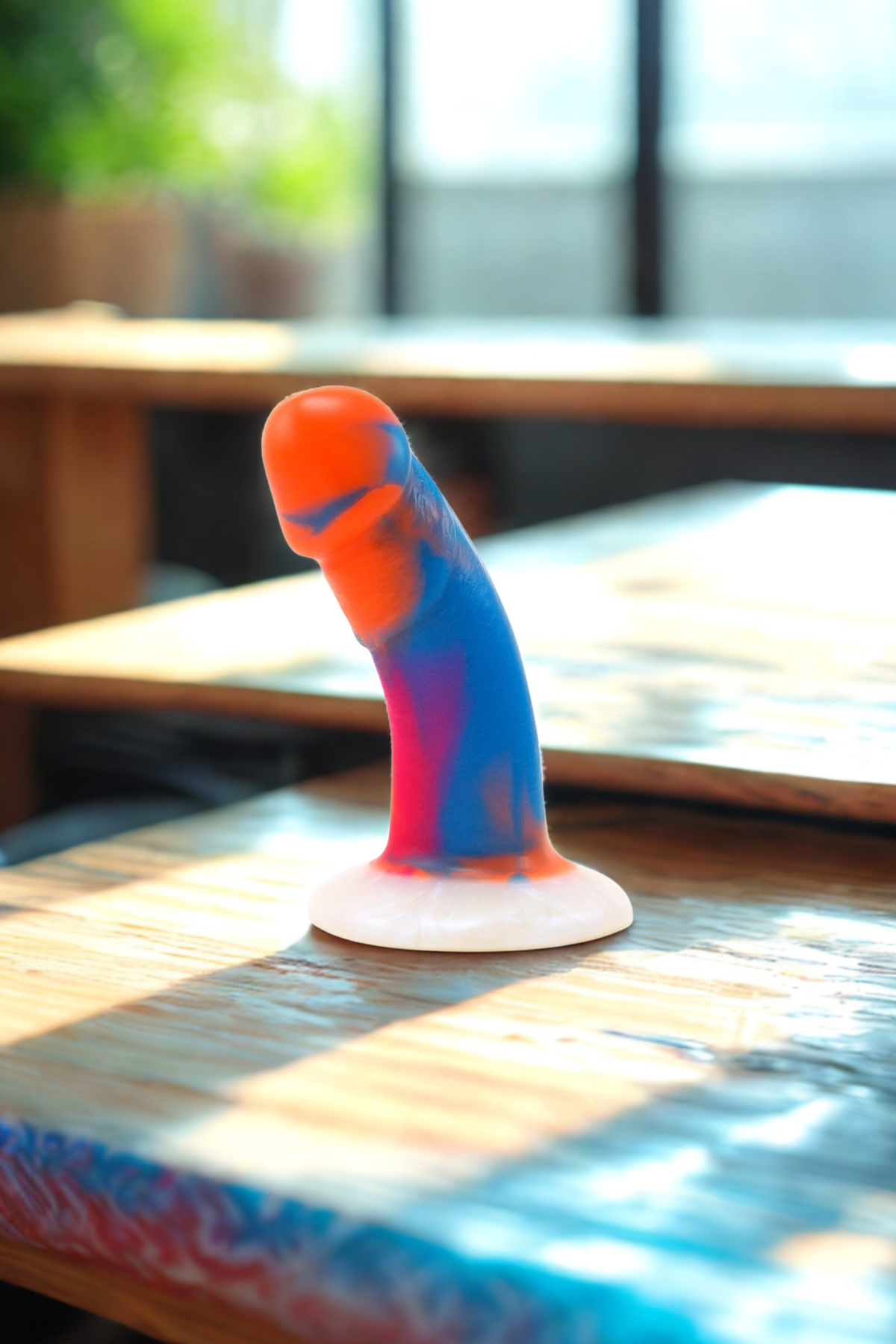 The marbled orange, blue and pink Tex standing upright on a paint splashed table top in a bright studio with a window behind it.