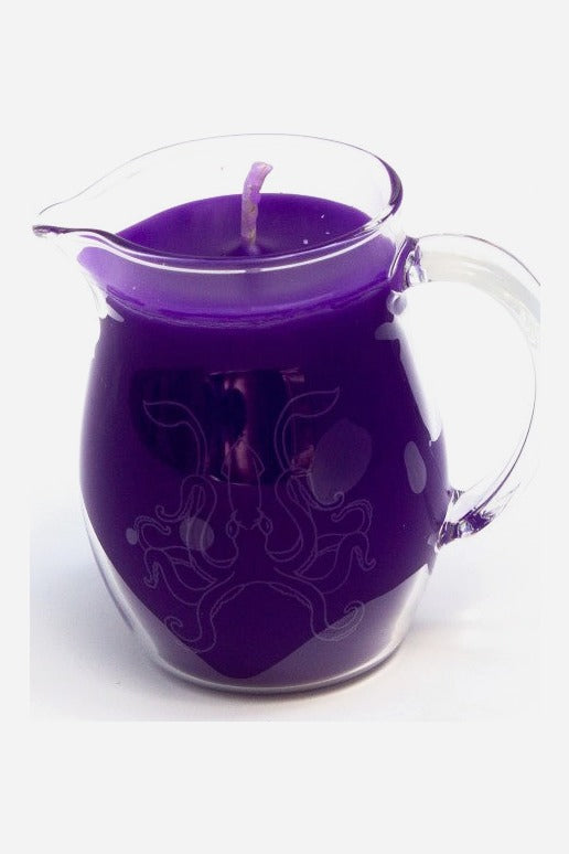 Glass pitcher candle with pour spout filled with purple low-temperature paraffin wax for wax play, shown on a light grey background