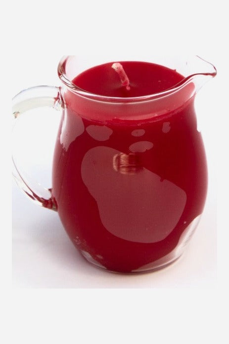 Red wax play pitcher candle: a clear glass jug with handle and pour spout filled with red unscented paraffin wax, on light grey