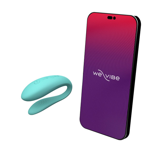 c-shaped wearable sex toy in aqua next to a cell phone with a we-vibe logo on its screen. meant to show that the sex toy can be controlled via the phone app