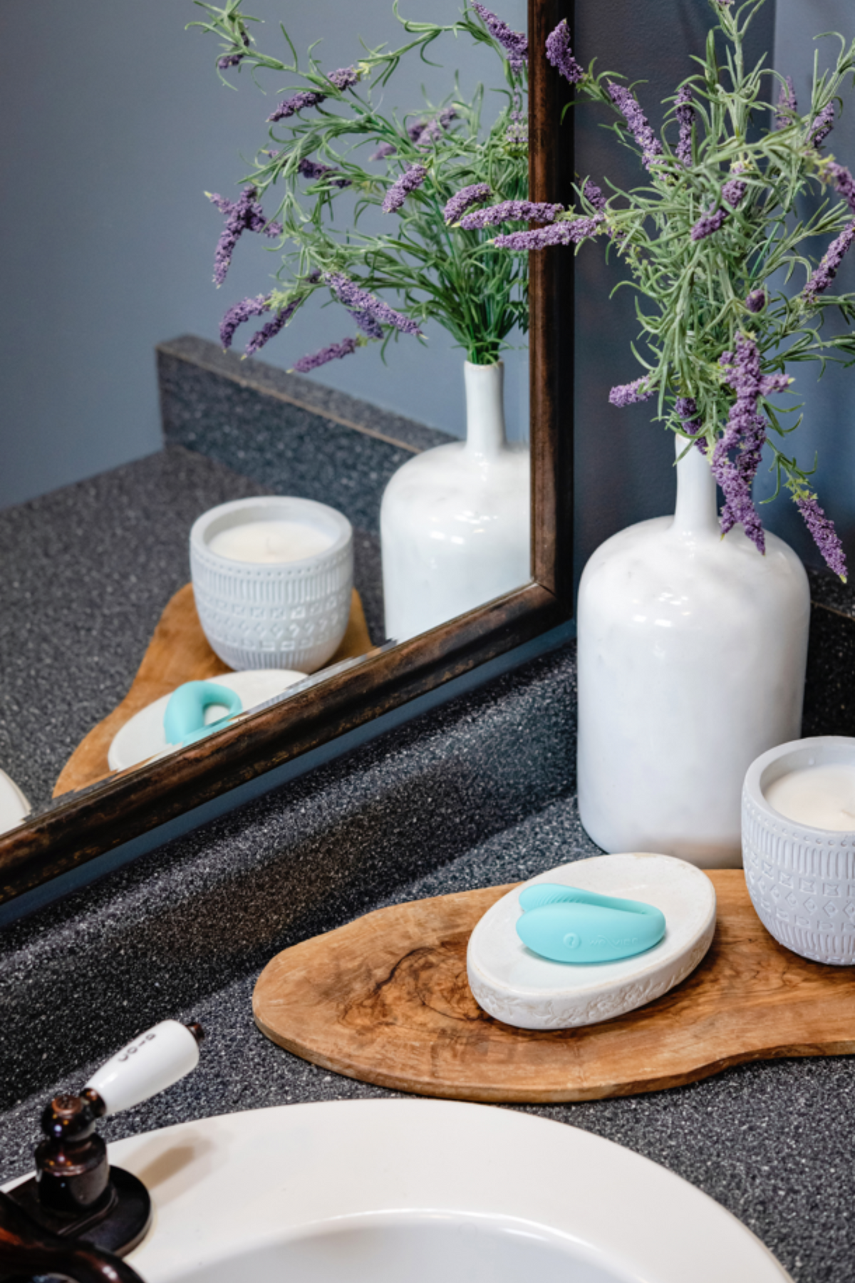 We-Vibe Sync Lite couples vibrator in Aqua on a stone dish beside a bathroom sink with candles, lavender and a mirror
