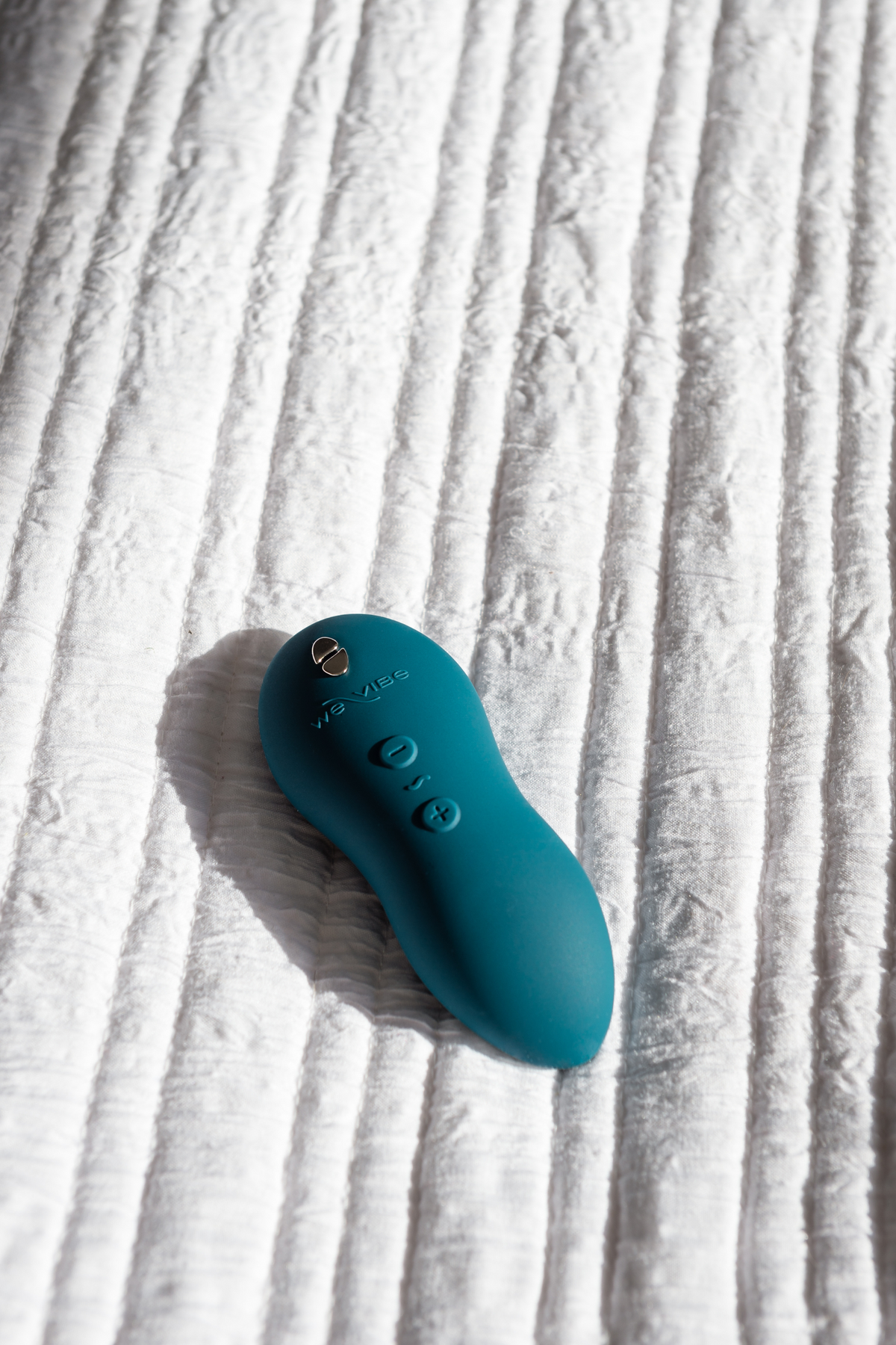 Green velvet We-Vibe TouchX resting on a white ribbed bedspread, showing the control buttons on this compact waterproof lay-on vibrator