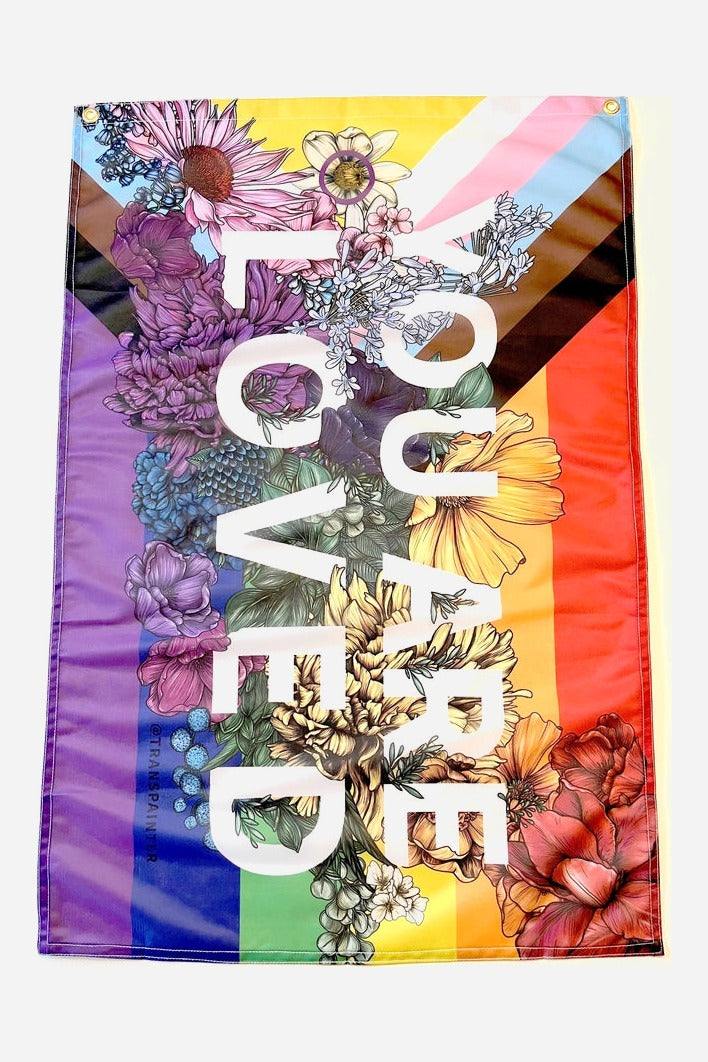 You Are Loved progressive pride flag by Transpainter, rainbow and trans stripes with hand-drawn flowers and white YOU ARE LOVED text