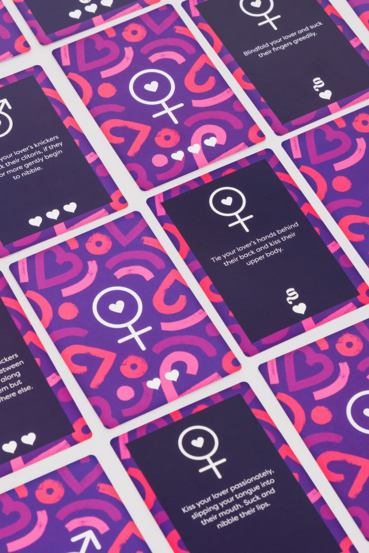 Challenge cards from the You and Me game spread out face up, each printed with a gender symbol and a short bedroom dare to carry out.