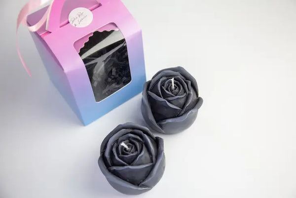 two black colored rose shaped candles with their pink and blue box