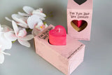 heart pillar shaped wax play candle sits in it's box. demonstrates how the box is used as a holder to catch drips
