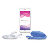 egg shaped panty vibe sex toy in periwinkle blue next to a cell phone. meant to show that the sex toy can be controlled via the phone app. there is also a charging cord to show that the toy is rechargeable via magnetic charger